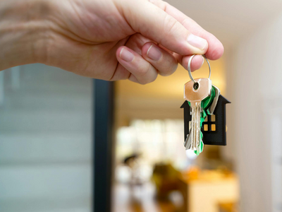 Hand hält Schlüsselbund mit kleinem Hausanhänger vor geöffneter Wohnungstür – Symbolbild für Immobilienkauf und Wohnbauförderung in Südtirol ab 2026